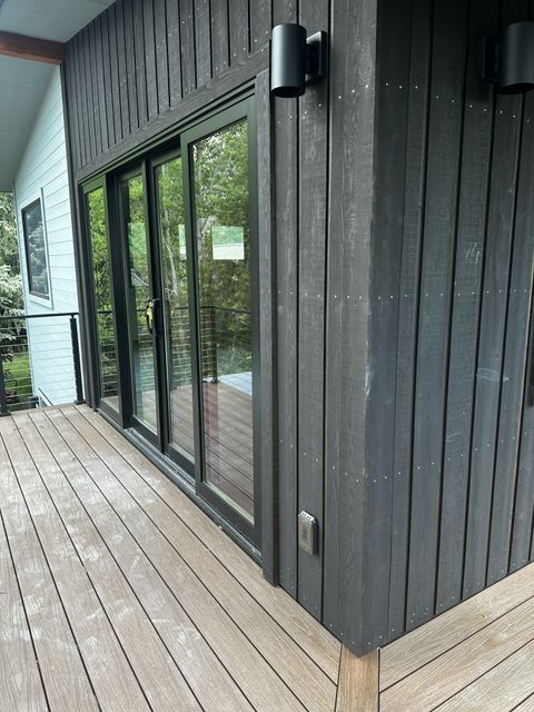 Wood deck along dark vertical siding and sliding glass doors